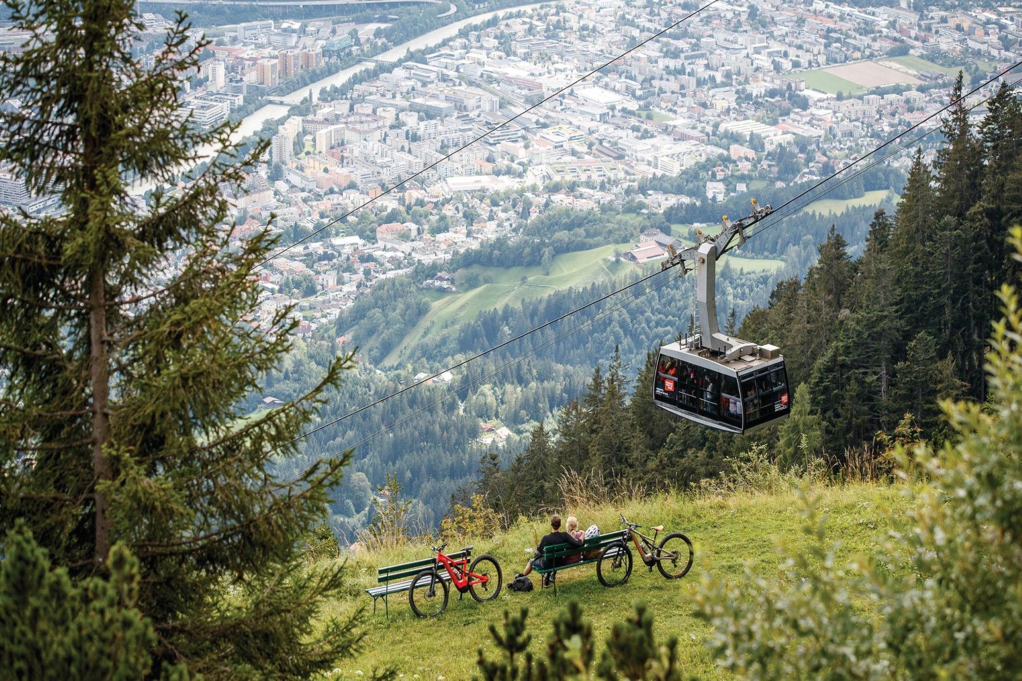 Funivia su colline verdi con vista su Innsbruck e biciclette in primo piano.